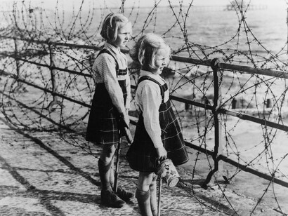 Due bambine guardano il mare al di là della rete di filo spinato
