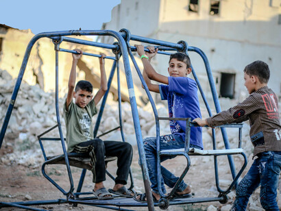 In the shattered remains of a war-torn city, poor children play among crumbling ruins and destroyed buildings