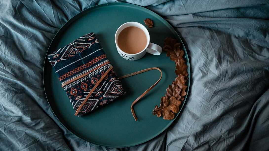 Una libreta de notas cerrada y vacía, junto a una tasa de café