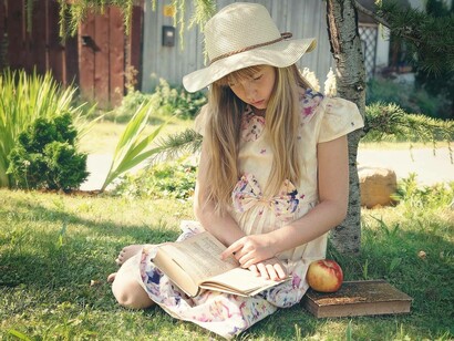 A young girl reading a lengthy book in her garden on a bright and sunny day