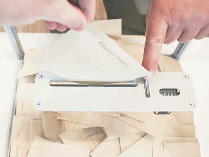 A voter places their ballot carefully in the box as the pollsters await to tabulate the results