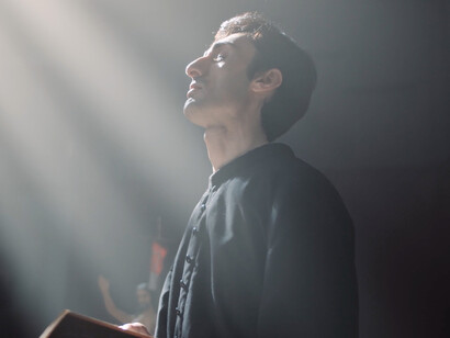 In the stillness of the cathedral, the priest's presence highlights the ongoing struggle between genuine spirituality and the exploitation of belief for commercial and political gain