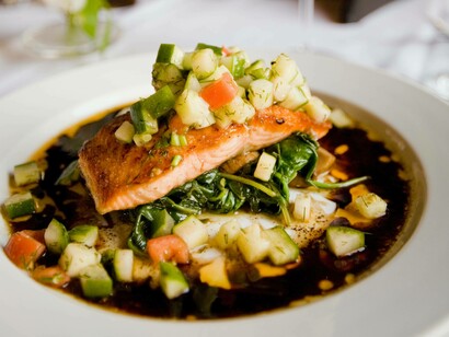 Delectable salmon on a bed of vegetables  surrounded by a vinaigrette jus that is artistically pleasing to the eye