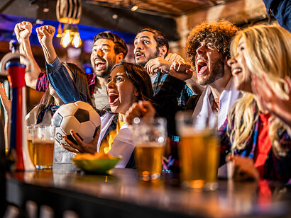 Excited football fans cheering and drinking beer while watching a match in a crowded pub