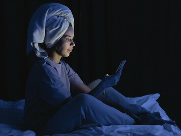 A woman illuminated by her phone screen in a dark bedroom, representing the cognitive overstimulation that lingers beyond scrolling