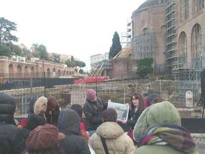 Simona Fanini explaining at the Imperial forum holding with a diagram of The Temple of Peace with the Basilica of Maxentius behind her