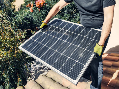A man in a black shirt installs a solar panel on a rooftop