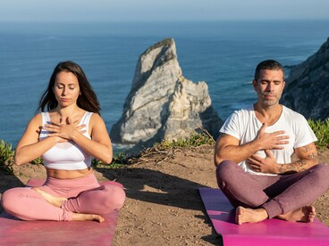 A man and woman practicing slow, mindful breathing in a peaceful coastal setting, symbolizing the connection between breath and emotional balance