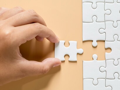 A human hand carefully places the final white puzzle piece into its designated spot on a nearly completed jigsaw, showing that each problem has a solution