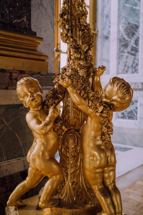 A golden statue of standing babies adorns the Palace of Versailles, adding a touch of whimsical grandeur to the opulent surroundings, France