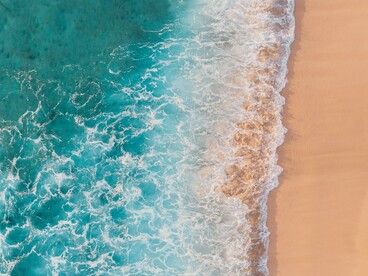As ondas avançam sobre a areia em uma faixa contínua de espuma, vista de cima. O movimento permanente da água dialoga com a ideia de transformação e com a necessidade de abandonar padrões que já não fazem sentido