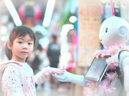 A young girl holds the hand of a robot holding a tablet computer