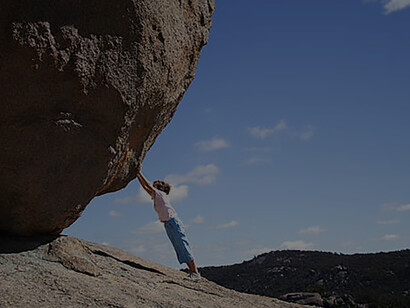 A little boy tries to push the huge boulder