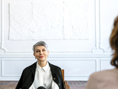A female psychologist in a black suit sits on a wooden chair during a couple’s therapy session