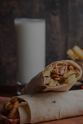 Side view of a delicious Turkish doner kebab shawarma, accompanied by golden fried potatoes, ayran, and a dollop of mayonnaise, elegantly presented on a wooden board