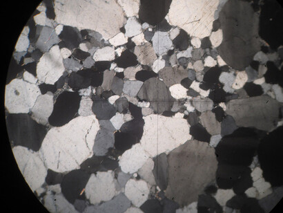 Arenisca: observada al microscopio petrográfico mediante luz polarizada. La cruz tiene de lado a lado 3 milímetros, y la mayoría de los granos que se observan en esta muestra son de cuarzo