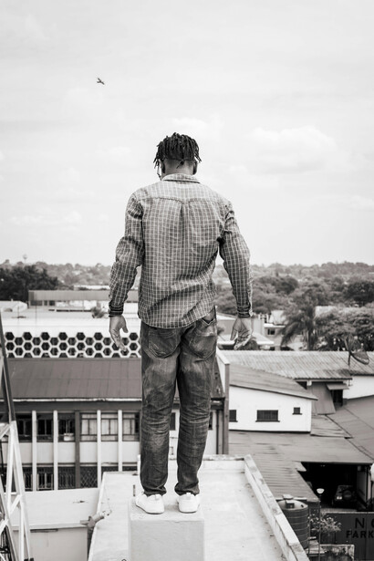 Homem na beira de prédio.Apoiado nos calcanhares, num rebordo minúsculo onde se cravam os parafusos e com os braços esticados para trás a segurar-se no revestimento de madeira