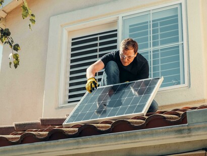 A man is installing a solar panel on the roof, contributing to renewable energy use