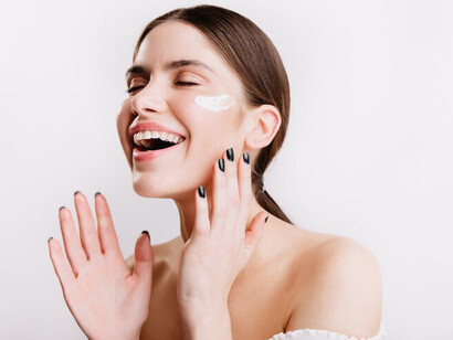 Smiling and with green eyes, a girl gently applies a soothing cream to her face, promoting self-care and using acne-fighting beauty products