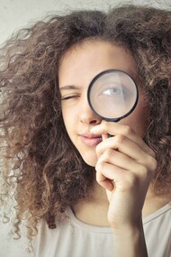 A portrait of a woman holding a magnifying glass over her eye