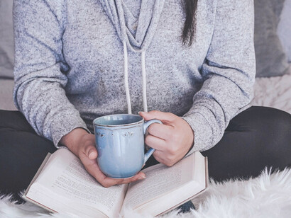 Un instant de tranquillité et de confort: des mains tenant une tasse et un livre, capturant l'essence de la joie des petits plaisirs de la vie quotidienne.