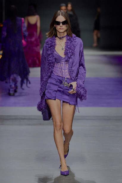 Modelo veste conjunto lilás com casaco, colares e óculos escuros