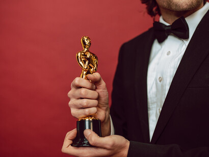 Dressed in a polished suit, a man exudes pure triumph while clutching a prestigious award, his elation reflecting both strength and enthusiasm, embodying the epitome of ambition and resounding success