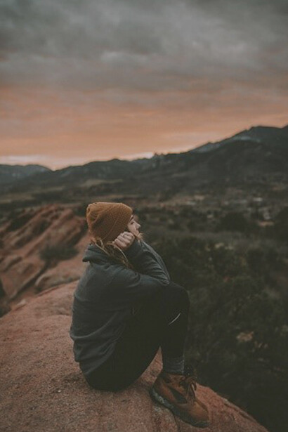 A woman, embodying the essence of feminine consciousness, sits gracefully on the rocks amidst the hills, embracing the interconnectedness of her inner landscape with the natural world around her