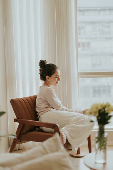 A woman journals in a warm, cozy apartment, tending to her inner healing and resting in gentle relaxation