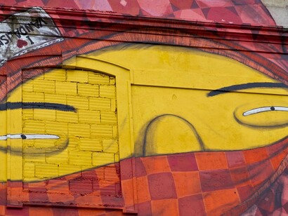 Obra sem título, mas reconhecida pelo nome "I love vandalismo", de Os Gêmeos, realizada em 2010 na Avenida Fontes Pereira de Melo, em Lisboa, Portugal. O detalhe evidencia o rosto amarelo do personagem encapuzado, cercado por formas vermelhas e geométricas que se integram à arquitetura do edifício. A intervenção faz parte do Projeto CRONO, que levou a arte urbana de grande escala para fachadas degradadas da capital portuguesa