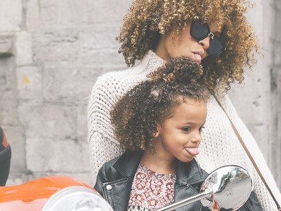 A carefree woman and her joyful daughter sticking out their tongues playfully beside a motorcycle