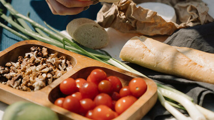 An assortment of healthy food on a table, including: cherry tomatoes, nuts, leaks and sliced bread