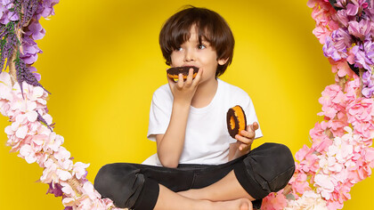 A cute boy enjoying donuts surrounded by flowers on a vibrant yellow desk