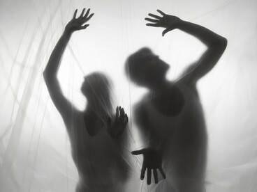 Two people concealed behind a curtain-like veil, reflecting the eerie pull of the supernatural