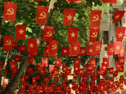 Bandeiras com símbolos comunistas penduradas de forma decorativa em uma rua, compondo um cenário marcado pela expressão política em espaço público. No artigo, a imagem dialoga com as reflexões do autor sobre ideologias, polarização e os desafios éticos e morais que, em sua visão, marcam a sociedade contemporânea