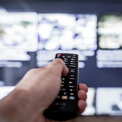 El mando apunta hacia una pantalla cargada de contenidos, símbolo de una audiencia que selecciona, cambia y consume información a un ritmo cada vez más inmediato