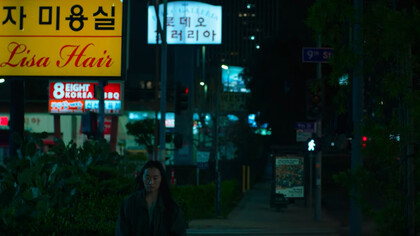 Lead character Hayoung walking alongside a downtown avenue at night in So Young Shelly Yo's ''Smoking Tigers''