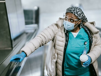 A Black nurse in a mask rides the underground escalator, unnoticed