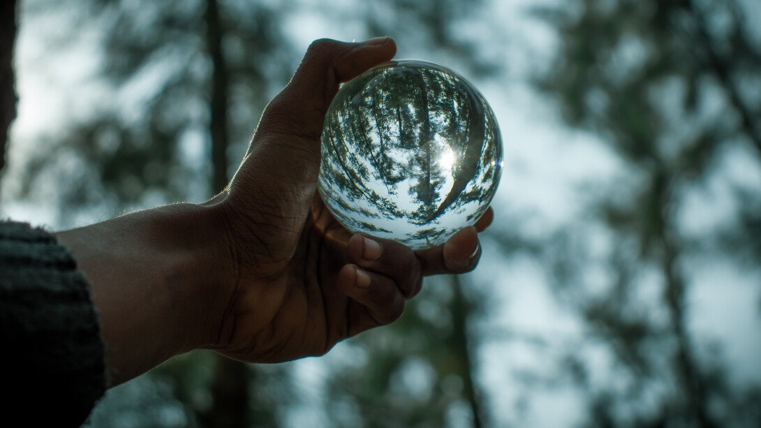 Homem enxerga floresta através do reflexo em uma pequena bola de vidro