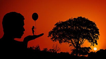 An illusion of a woman holding a balloon on the hand of a man during a sunset as he looks at her with awe at her confidence