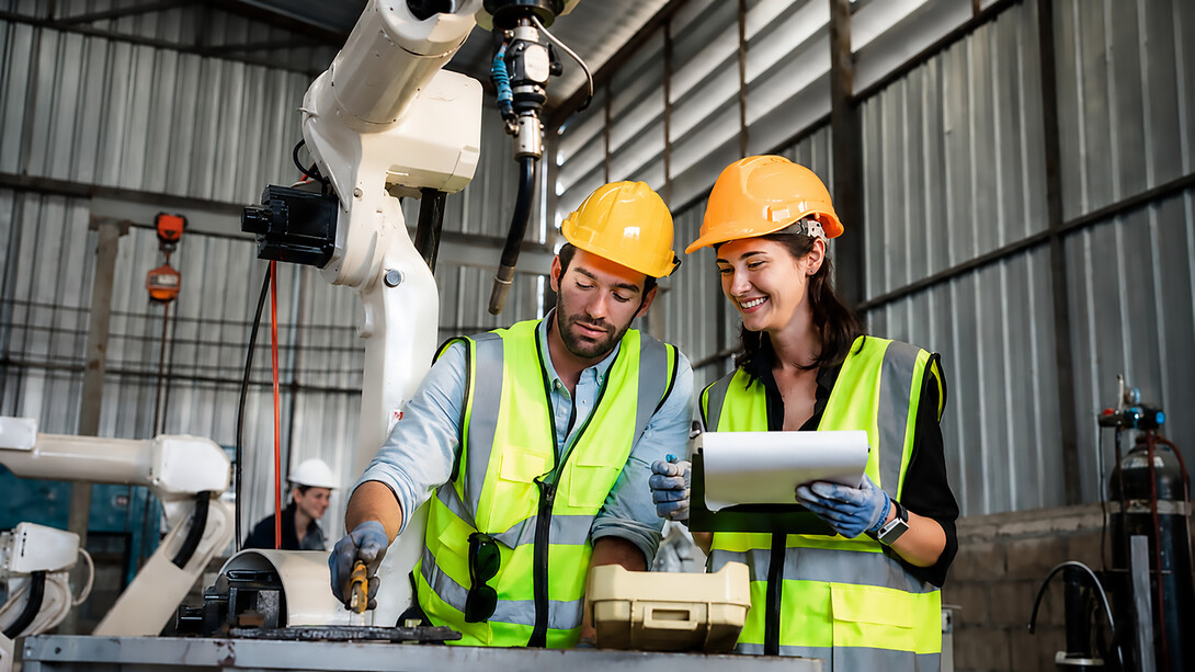 Industrial engineers overseeing automated robotic arms welding steel components in a modern manufacturing facility