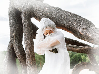A woman wrapped in plastic, with a mask, hugging a tree