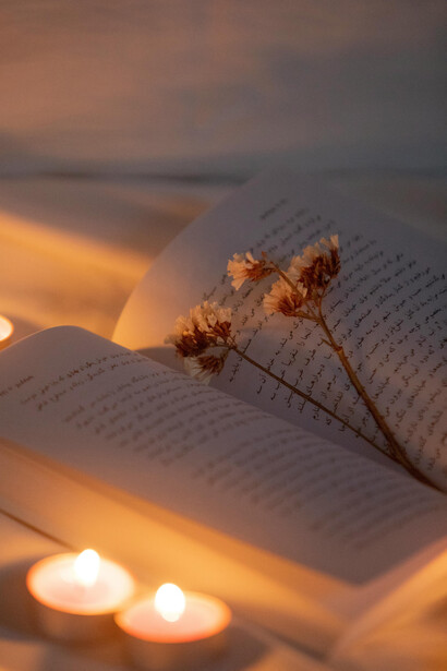Un libro con unas pequeñas flores arriba y velas iluminando. Los poetas y escritores utilizan la metáfora de la petite mort para explorar la complejidad de las relaciones humanas y la efímera naturaleza del deseo