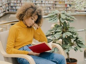 Jovem lendo um livro sozinha na biblioteca