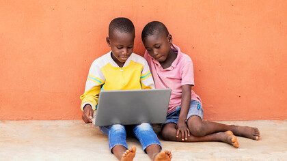 Children gather around a laptop in a rural African community, where limited internet access poses a barrier to education and development