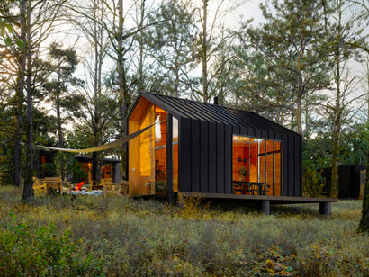 Exterior view of a wooden tiny house with a forest backdrop, showcasing prefabricated buildings and factory-built modules in prefab architecture