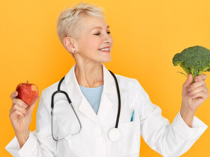 An energetic middle-aged woman physician with a stethoscope around her neck smiles excitedly beside her happy senior patient