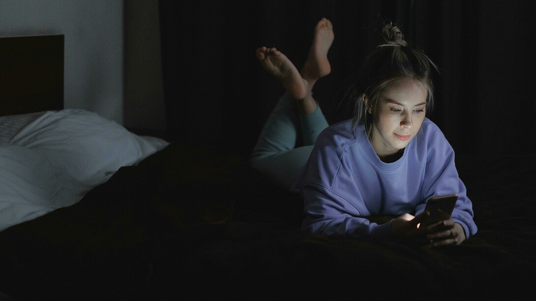 A woman lying on a bed while scrolling through social media on her cellphone, illustrating digital addiction