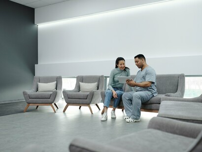 A clinic waiting room where a medic speaks with a patient, reflecting the hidden burden of waiting for essential healthcare services