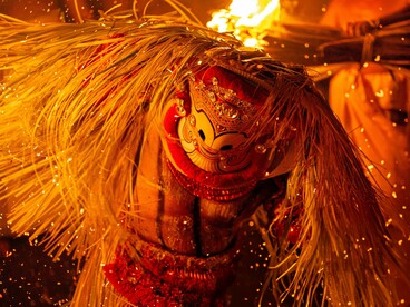A Theyyam performer illuminated by firelight during a sacred ritual, representing Kerala's vibrant traditions and centuries-old cultural heritage